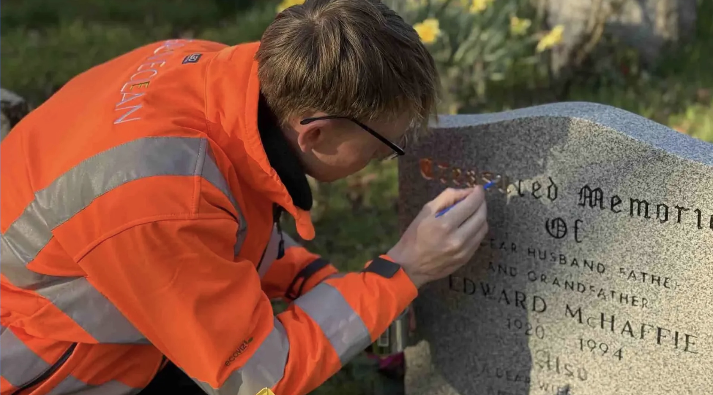 A monumental mason restoring the gilded lettering on a granite headstone